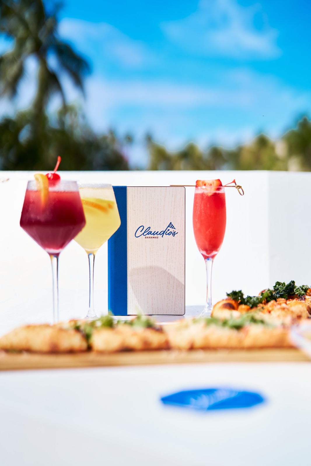 Cocktails around the Claudio's Bahamas menu under palm trees
